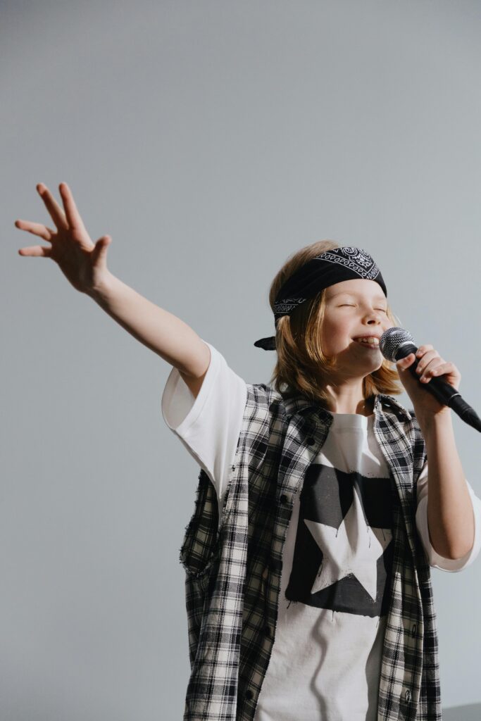Joyful child singing with a microphone, wearing a bandana and plaid shirt, against a neutral background.